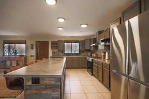 Kitchen featuring a center island, tasteful backsplash, appliances with stainless steel finishes, light tile patterned flooring, and wall chimney range hood