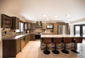 Kitchen with a breakfast bar area, a kitchen island, a sink, stainless steel appliances, and wall chimney range hood