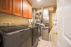 Washroom featuring washer and clothes dryer, gas water heater, cabinet space, and light tile patterned floors