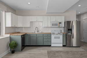 Kitchen with white cabinetry, butcher block counters, sink, white appliances, and decorative backsplash