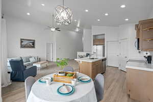 Dining space featuring ceiling fan with notable chandelier, light hardwood / wood-style flooring, sink, and vaulted ceiling