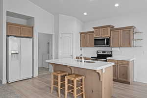 Kitchen featuring sink, stainless steel appliances, an island with sink, and light wood-type flooring