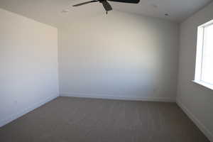 Carpeted empty room with a ceiling fan, baseboards, lofted ceiling, and visible vents