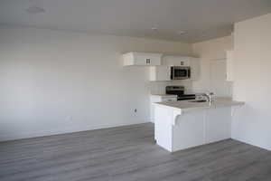 Kitchen featuring a sink, light countertops, white cabinets, stainless steel appliances, and a peninsula