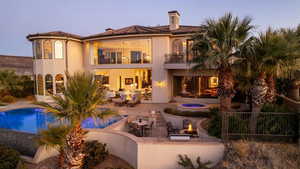 Back of house at dusk with a balcony, a chimney, an outdoor pool, a patio area, and an outdoor fire pit