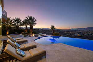 View of pool featuring an infinity pool, a patio, a mountain view, and an in ground hot tub