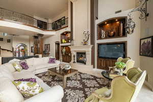 Living room with a towering ceiling, a large fireplace, ornate columns, and arched walkways