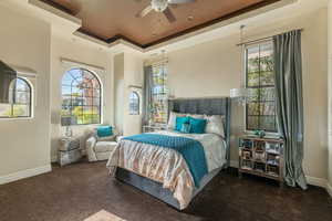 Bedroom with ceiling fan, baseboards, dark colored carpet, and a tray ceiling