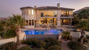 Back of house at dusk with a balcony, a patio, a tiled roof, and a fenced in pool