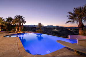 Pool at dusk featuring an infinity pool, a patio area, and a mountain view