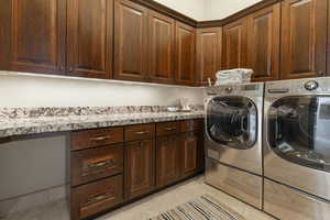 Clothes washing area featuring light tile patterned floors, cabinet space, and washer and clothes dryer