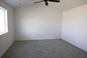 Empty room featuring ceiling fan, baseboards, visible vents, vaulted ceiling, and dark colored carpet