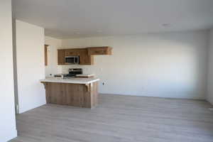 Kitchen with light countertops, stainless steel appliances, a peninsula, brown cabinets, and light wood finished floors