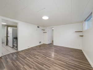 Basement featuring stacked washer / drying machine, dark hardwood / wood-style floors, and white refrigerator