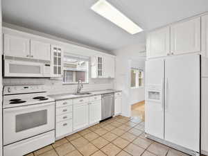 Kitchen with light tile patterned flooring, white cabinetry, sink, backsplash, and white appliances