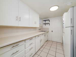 Kitchen with sink, white cabinetry, stacked washer and clothes dryer, white refrigerator, and light tile patterned flooring