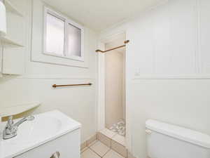 Bathroom with vanity, a tile shower, tile patterned floors, and toilet