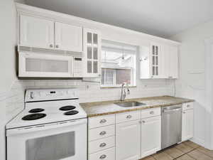 Kitchen featuring sink, white appliances, light tile patterned floors, white cabinetry, and backsplash