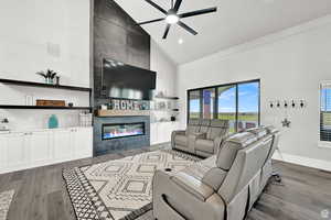 Living room featuring a fireplace, high vaulted ceiling, dark wood-style floors, and a healthy amount of sunlight