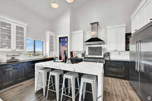 Kitchen with glass insert cabinets, high end fridge, a center island, and wall chimney range hood