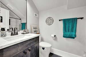 Full bath with vanity, toilet, visible vents, and vaulted ceiling