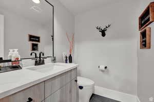 Half bath with visible vents, vanity, baseboards, and toilet