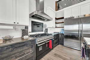 Kitchen featuring wall chimney range hood, white cabinetry, dark countertops, and high end appliances