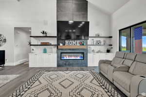 Living room featuring baseboards, high vaulted ceiling, a tiled fireplace, and wood finished floors