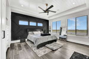 Bedroom featuring multiple windows, a tray ceiling, and wood finished floors