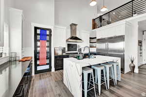 Kitchen with open shelves, a kitchen island with sink, decorative light fixtures, wall chimney range hood, and white cabinets