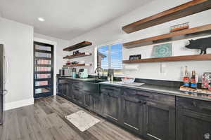 Kitchen featuring a sink, recessed lighting, light wood finished floors, dark cabinets, and open shelves