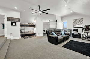 Living room with ceiling fan, vaulted ceiling, light colored carpet, a barn door, and a textured ceiling