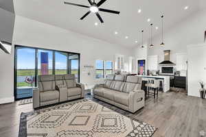 Living room with high vaulted ceiling, baseboards, ceiling fan, and light wood-type flooring