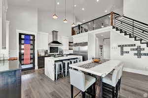 Kitchen featuring a breakfast bar, white cabinetry, a kitchen island with sink, built in fridge, and wall chimney range hood