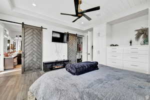 Bedroom featuring ceiling fan, light wood-style floors, a barn door, recessed lighting, and a tray ceiling