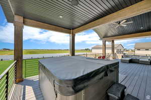 Wooden terrace with fence, a ceiling fan, a lawn, and a hot tub