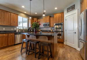 Kitchen featuring a kitchen island, stainless steel appliances, hardwood / wood-style floors, and decorative light fixtures