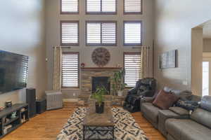 Living room featuring light wood-type flooring, a wealth of natural light, a high ceiling, and a stone fireplace