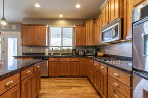 Kitchen with dark stone countertops, appliances with stainless steel finishes, sink, decorative light fixtures, and light hardwood / wood-style floors