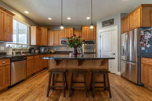 Kitchen featuring appliances with stainless steel finishes, a kitchen breakfast bar, decorative light fixtures, a center island, and light wood-type flooring