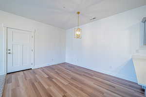 Empty room featuring baseboards, visible vents, an inviting chandelier, and wood finished floors