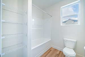 Full bath with toilet, shower / washtub combination, wood finished floors, and baseboards