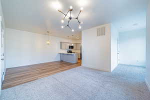 Unfurnished living room with baseboards, visible vents, light colored carpet, and a notable chandelier