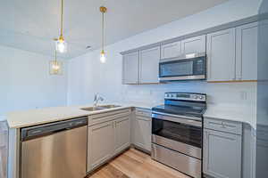 Kitchen with a sink, light countertops, appliances with stainless steel finishes, decorative light fixtures, and a peninsula