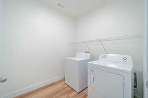 Washroom with independent washer and dryer, baseboards, visible vents, light wood-style floors, and laundry area