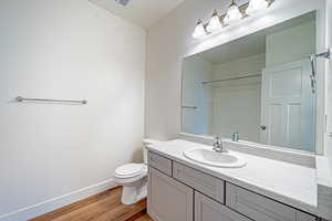 Bathroom featuring vanity, wood finished floors, baseboards, toilet, and walk in shower