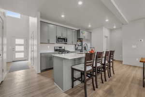 Kitchen with a kitchen bar, stainless steel appliances, gray cabinetry, and a kitchen island with sink