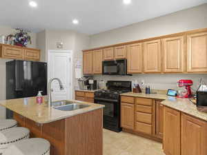 Kitchen with sink, light stone counters, a kitchen breakfast bar, black appliances, and a kitchen island with sink