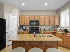 Kitchen with an island with sink, black appliances, light stone countertops, and a breakfast bar area