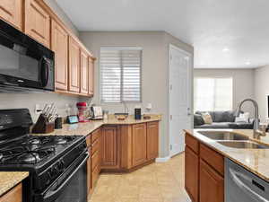 Kitchen with light tile patterned floors, sink, black appliances, and light stone counters